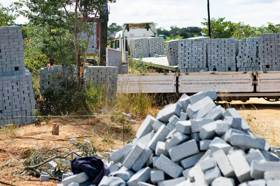 Un camión de plataforma cargado con tarimas de bloques de concreto en una obra, con un montón de bloques al frente