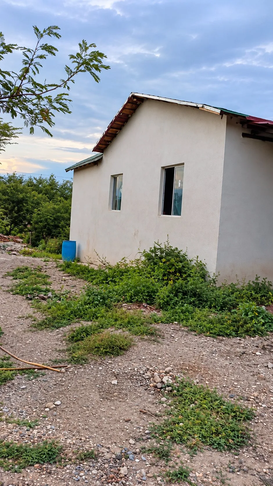 Una casa pequeña aplanada con dos ventanas y techo de lámina al atardecer
