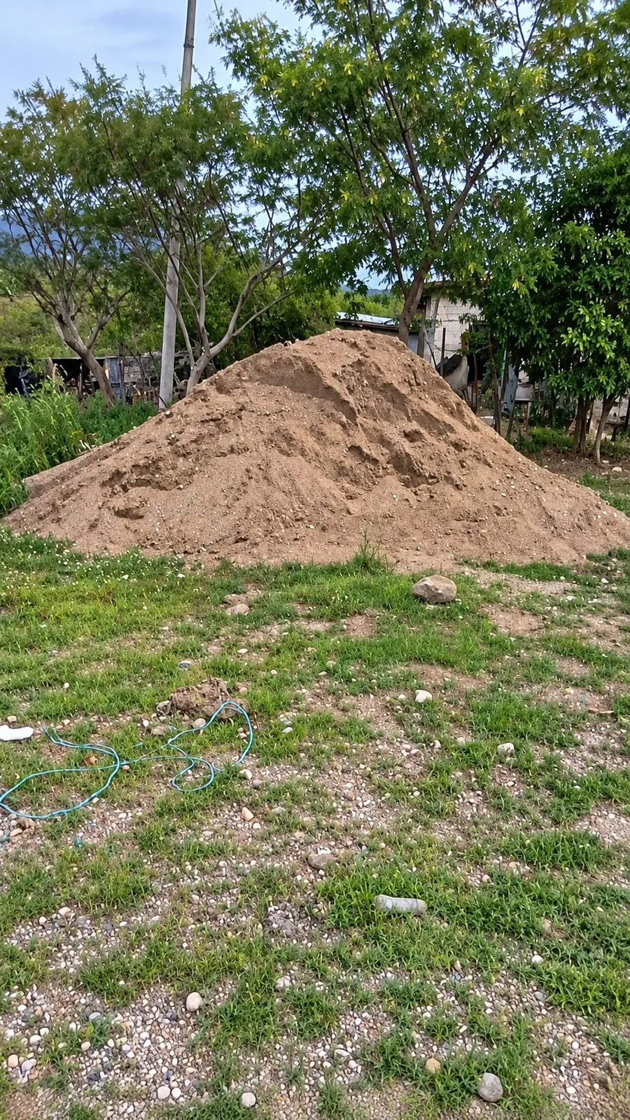 Un montón grande de arena en un terreno con pasto y árboles al fondo